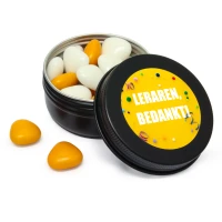 Zwart blikje met oranje en witte snoepjes en gele sticker voor het bedanken van de leraren